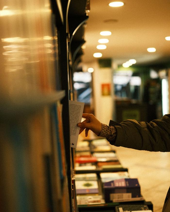 Hand greift nach einem Buch im Regal einer Buchhandlung, davor Auslagen mit Neuerscheinungen