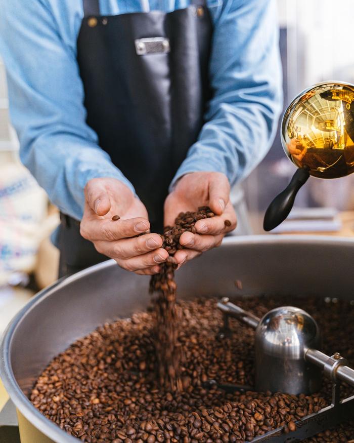 Zwei Hände lassen frisch geröstete Kaffeebohnen in die Trommel der Röstmaschine rieseln