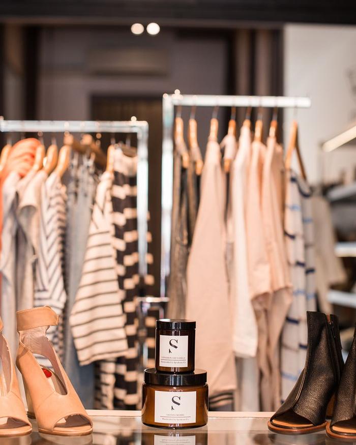 Blick in ein Modegeschäft mit Kleiderstangen, Schuhen und Duftkerzen auf der Theke